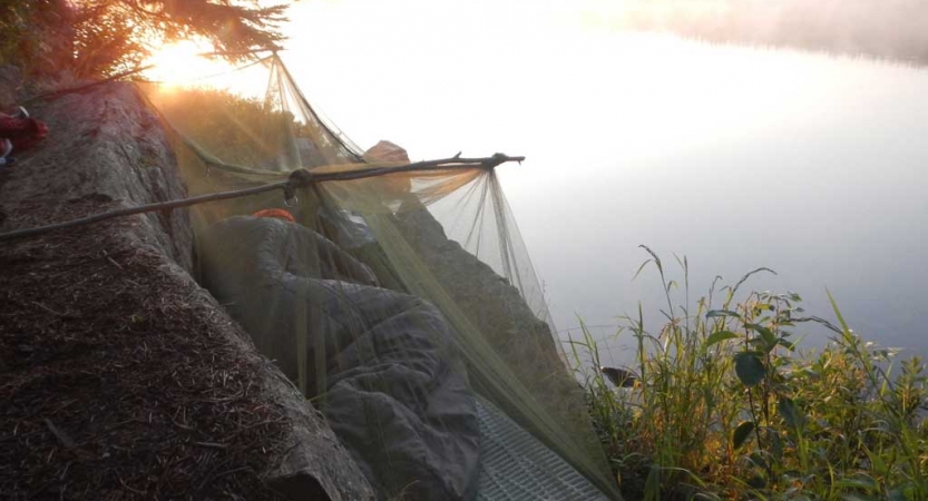 A person rests in a sleeping back on a cliff above a body of water.